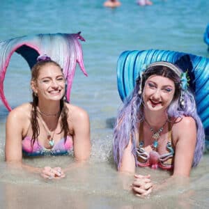 Two mermaid performers in the ocean at the beach
