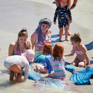 A mermaid performer in the ocean at the beach surrounded by children at a birthday party.