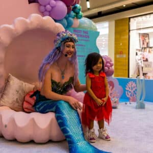 A mermaid performer posing with a child at a corporate event.