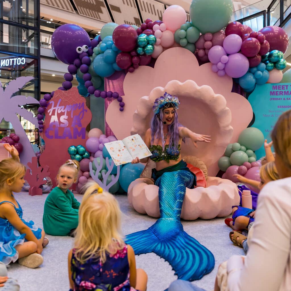 A mermaid performer reading a story book at a corporate event