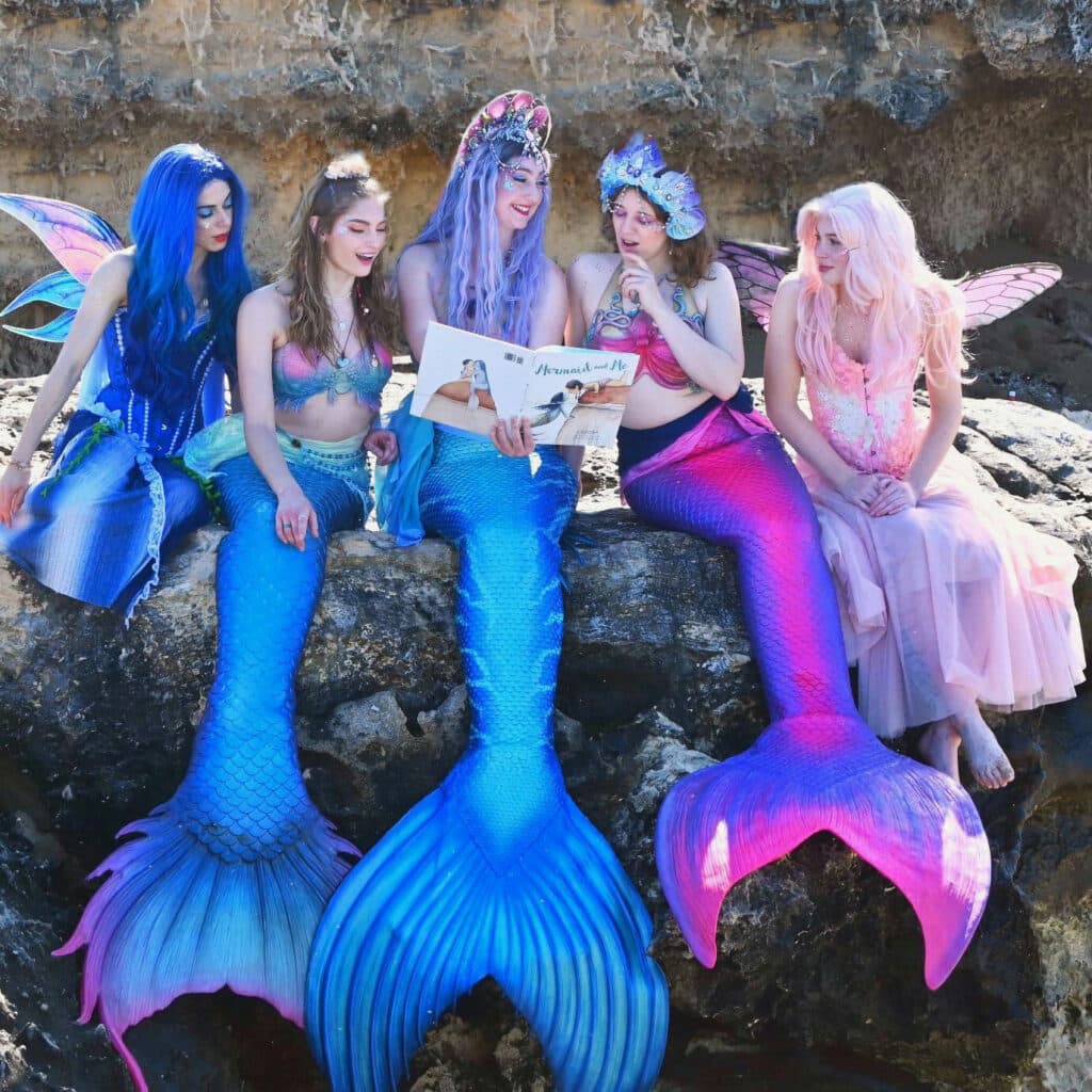 Mermaid and fairy performers ready a story book on the rocks