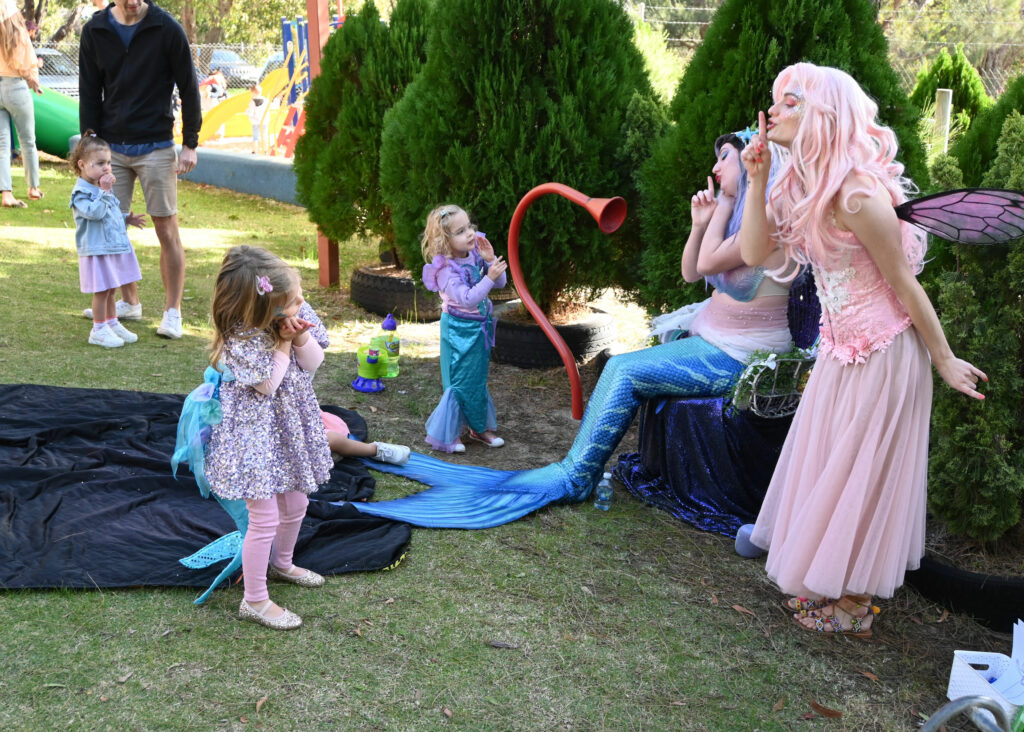 A mermaid and a fairy performer playing games with children at a birthday party