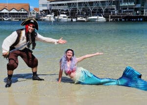 A mermaid and a pirate posing in the ocean at the beach